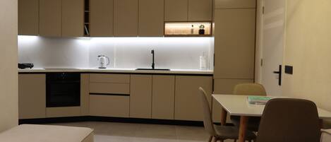 Una cocina moderna con electrodomésticos integrados, un comedor con mesa y sillas, y una zona de estar acogedora con otomanas.
