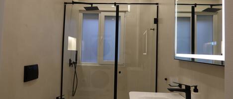 A modern bathroom with a glass-enclosed shower, a white sink, and a mirror above the sink.