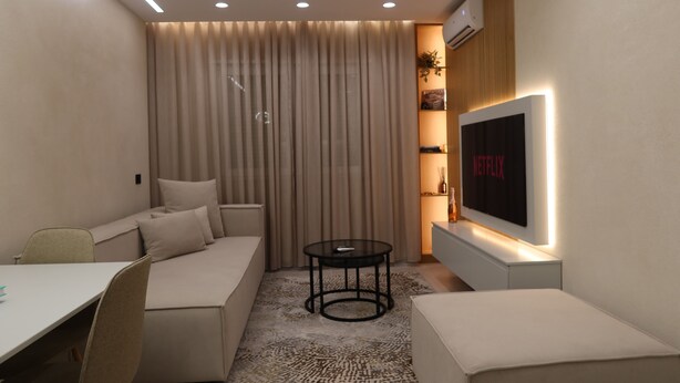 Una sala de estar moderna con un sofá, una mesita redonda, un televisor montado en la pared y un tapete estampado.