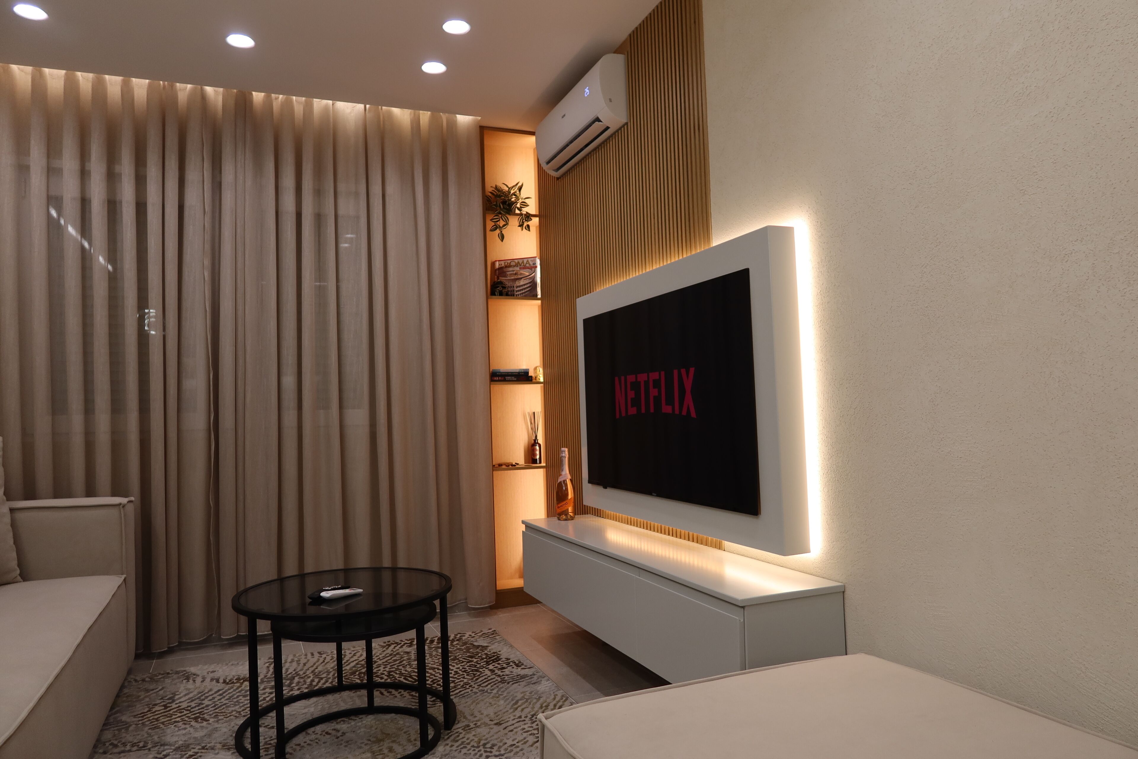A modern living room with a large flat-screen TV mounted on a wall, a sofa, a coffee table, and a decorative plant.