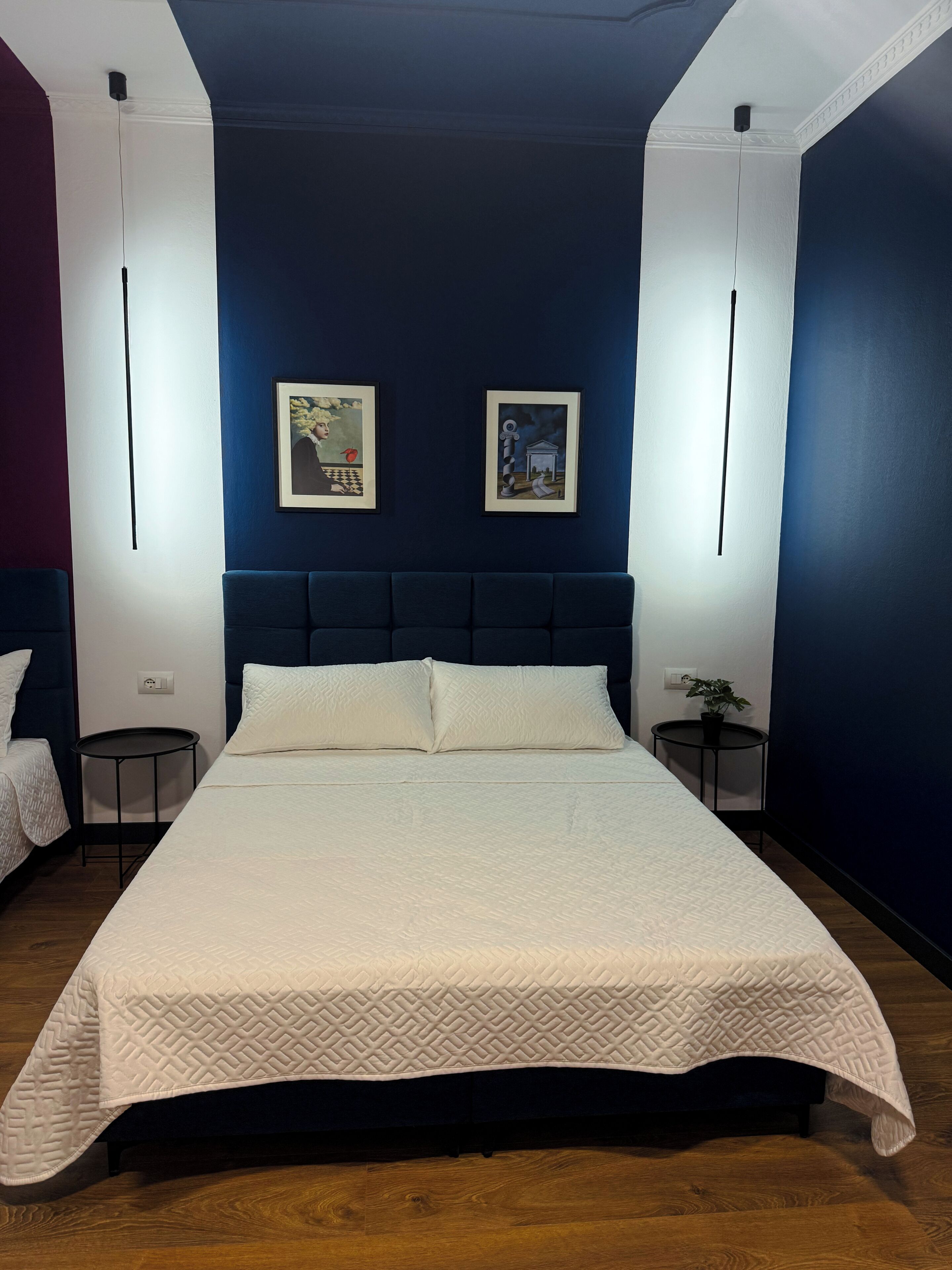 Une chambre à coucher moderne avec un grand lit, deux œuvres d’art encadrées accrochées au mur, une petite table ronde et une petite plante en pot.
