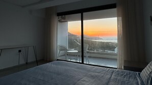 A bedroom with a large bed, a balcony with a view of the sunset, and a dining area with chairs. - Blue Lagoon duplex with views of cape blanc, sea 🌊, grotto beach and forest🌳 (Bizerte)