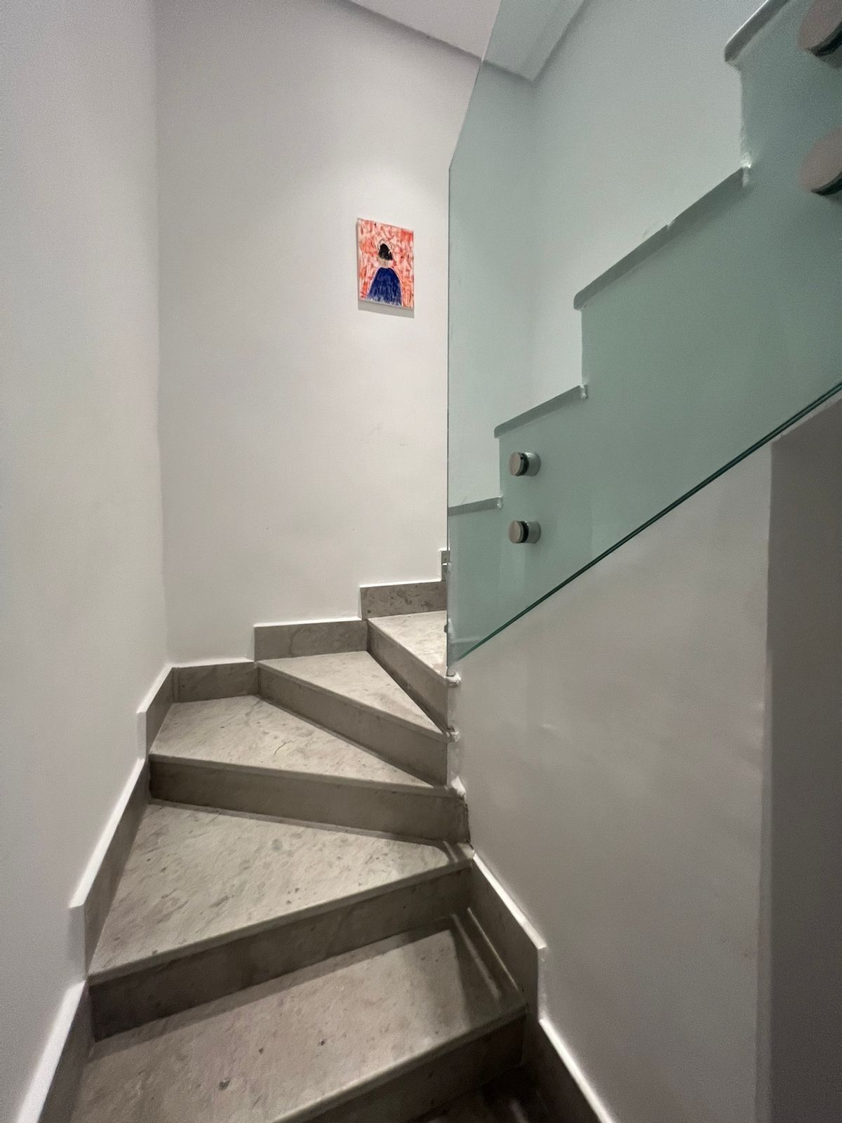 A staircase with a glass railing and a small artwork on the wall.