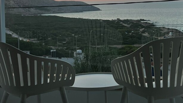 A balcony with two chairs facing a sunset view over a coastal landscape. - Blue Lagoon duplex with views of cape blanc, sea 🌊, grotto beach and forest🌳 (Bizerte)