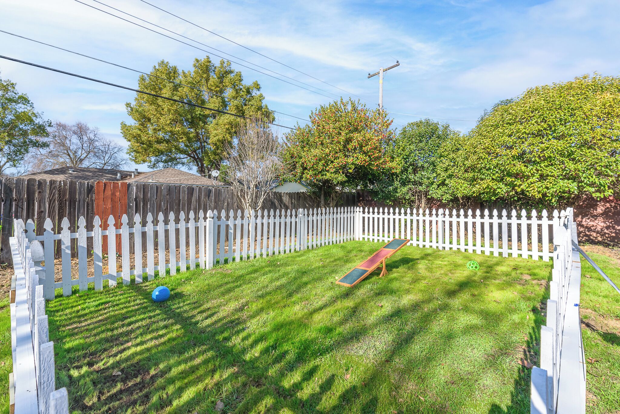 A well-maintained backyard with a wooden fence, a trampoline, and a lawn.