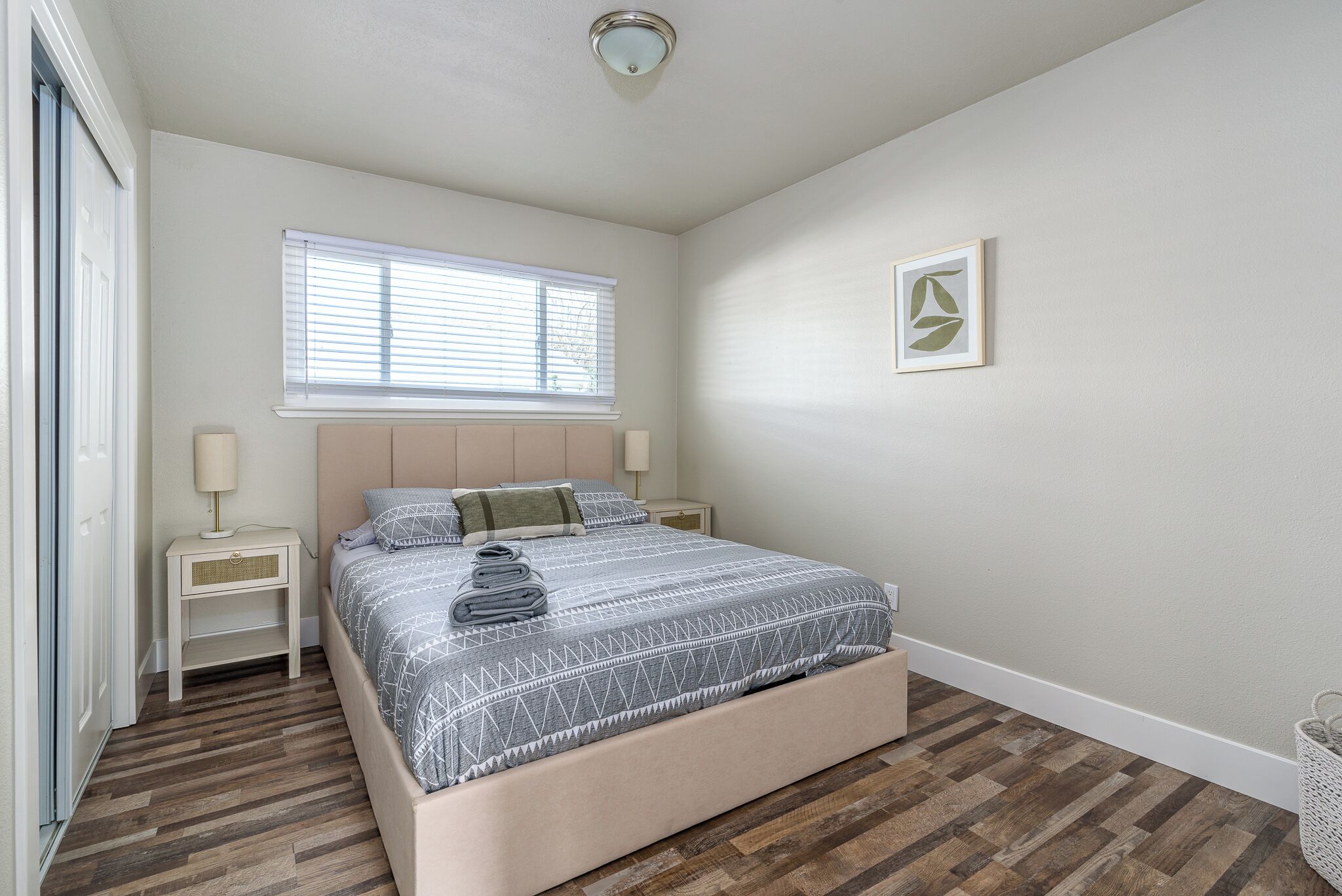 A bedroom with a bed, nightstands, a window, and a framed picture on the wall.