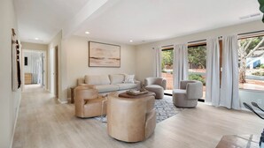 A spacious living room with a beige sofa, a round coffee table, and a large window with curtains.