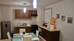A compact kitchen with wooden cabinets, a dining table with chairs, a refrigerator, and a microwave on the countertop. - Furnished apartment in downtown Guadalajara (Guadalajara)