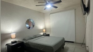 A bedroom with a bed, two bedside tables with lamps, a ceiling fan, a wall-mounted TV, and a door. - Furnished apartment in downtown Guadalajara (Guadalajara)