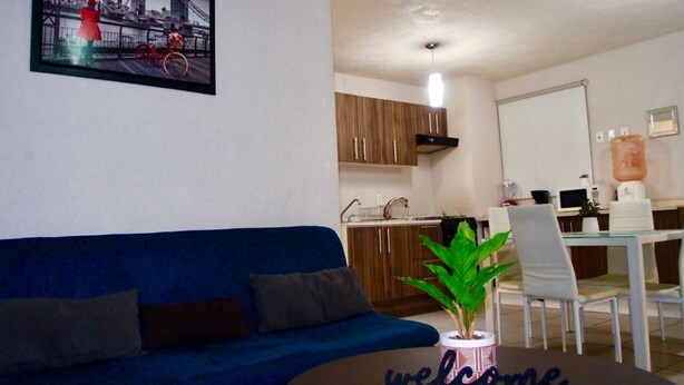 A modern living room with a blue sofa, a coffee table with a 'welcome' sign, and a dining area with white chairs and a glass table. - Furnished apartment in downtown Guadalajara (Guadalajara)
