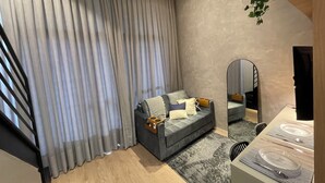 A modern living room with a grey sofa, a large mirror, and a dining area with a striped tablecloth. - Beautiful studio with mezzanine in Brooklyn (Jardim das Acacias São Paulo)