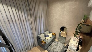 A modern bedroom with a grey sofa, a large mirror, and a potted plant. - Beautiful studio with mezzanine in Brooklyn (Jardim das Acacias São Paulo)