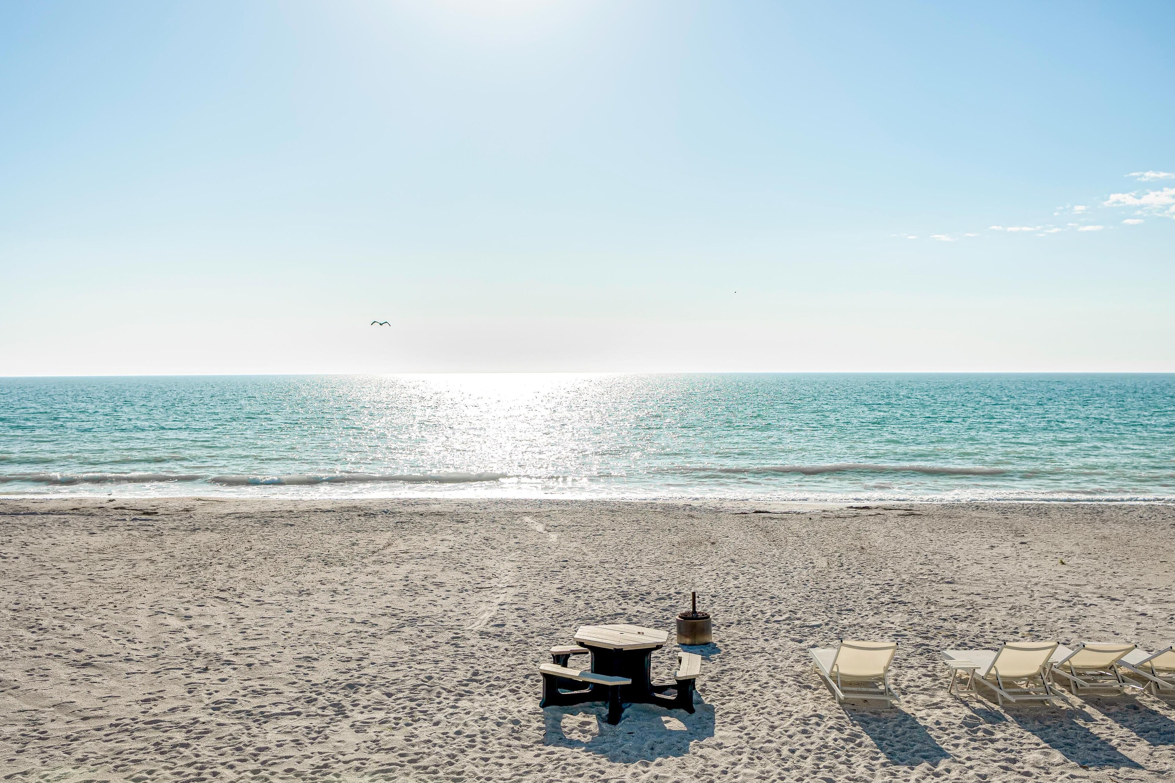 A beach with a wooden picnic table and lounge chairs facing the ocean.