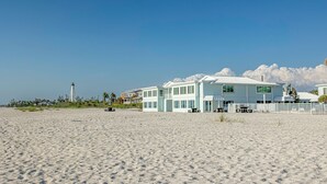A beachfront property with a large, light-colored house featuring multiple windows and a covered patio area.