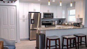 A modern kitchen with white cabinets, stainless steel appliances, a granite countertop, and bar stools.