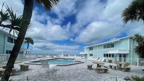 A pool area with lounge chairs, a pool, and a building with a light blue exterior.