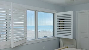 A room with a large window overlooking a beach, a bed, and a chair.