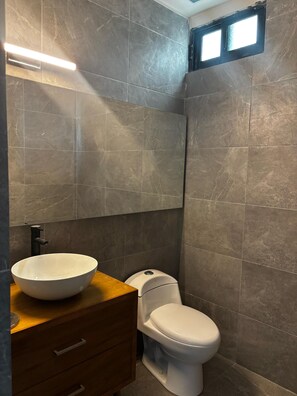 Un baño con un lavamanos blanco de diseño, un inodoro blanco y un mueble de tocador de madera.