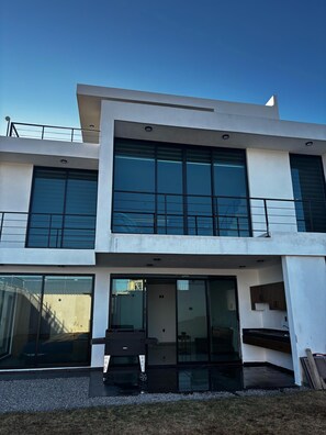 Una casa moderna de dos pisos con ventanas amplias, un garaje y un pequeño espacio al aire libre para sentarse.