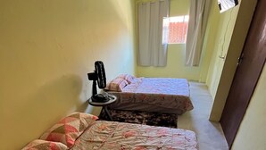 Een kleine, eenpersoonskamer met twee bedden, een ventilator en een aan de muur bevestigde televisie.