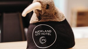 Un peluche con un chaleco negro que dice 'Auckland City Hotel'.