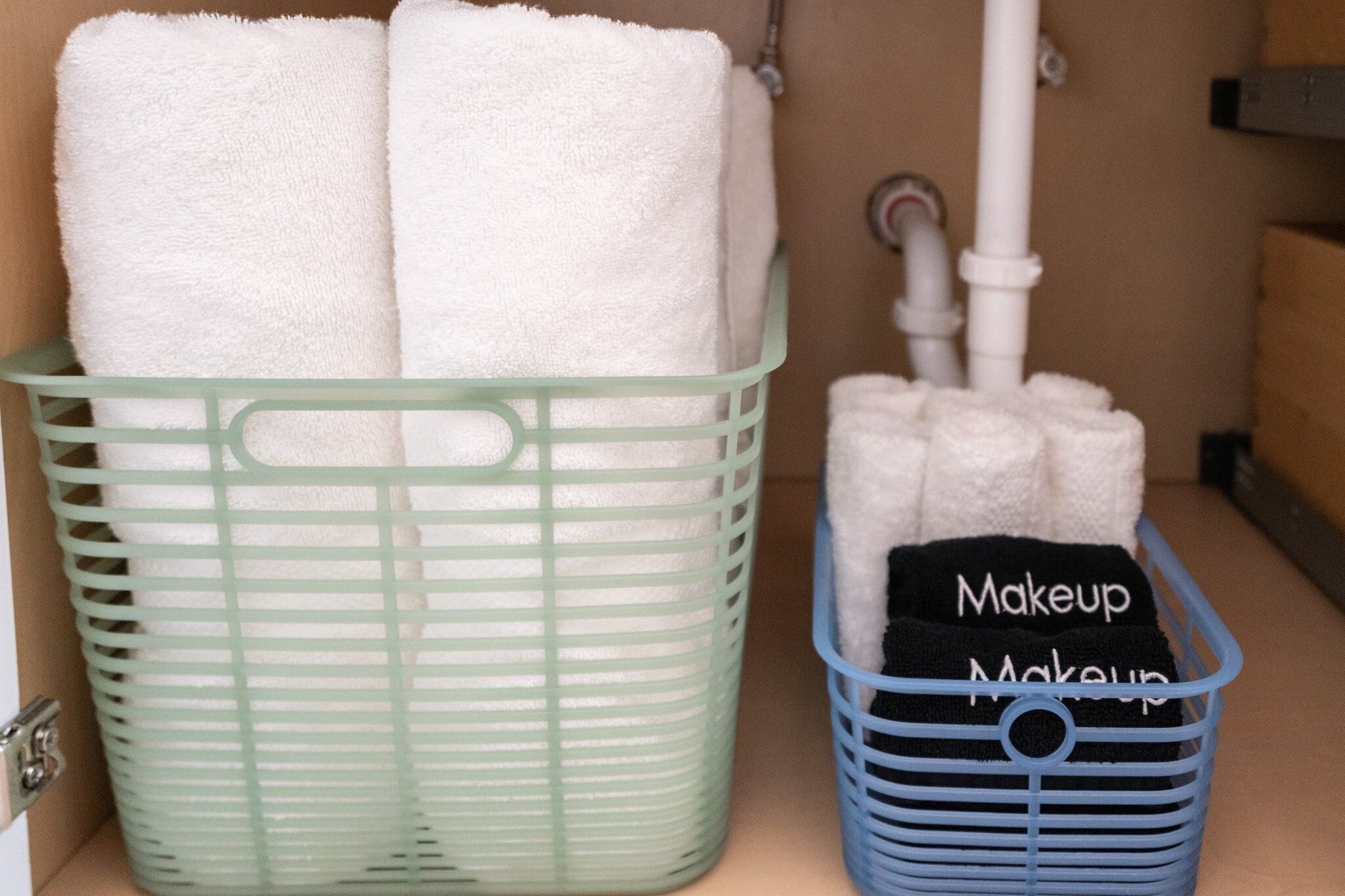 Un baño con un cesto verde para ropa que contiene toallas blancas y un cesto azul etiquetado como "Maquillaje" con toallas negras.