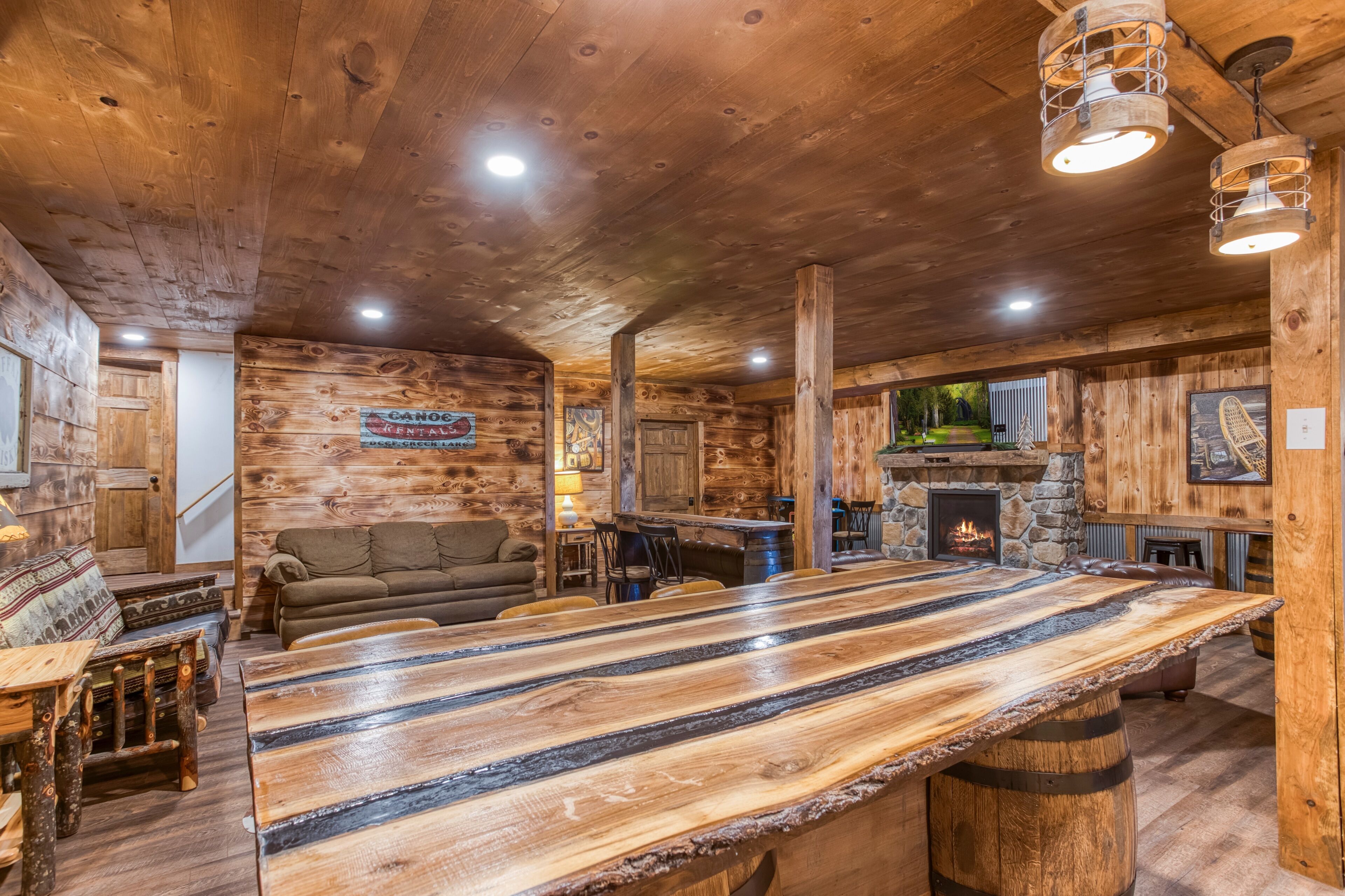 A rustic cabin interior with a large wooden bar, seating area, and a stone fireplace.