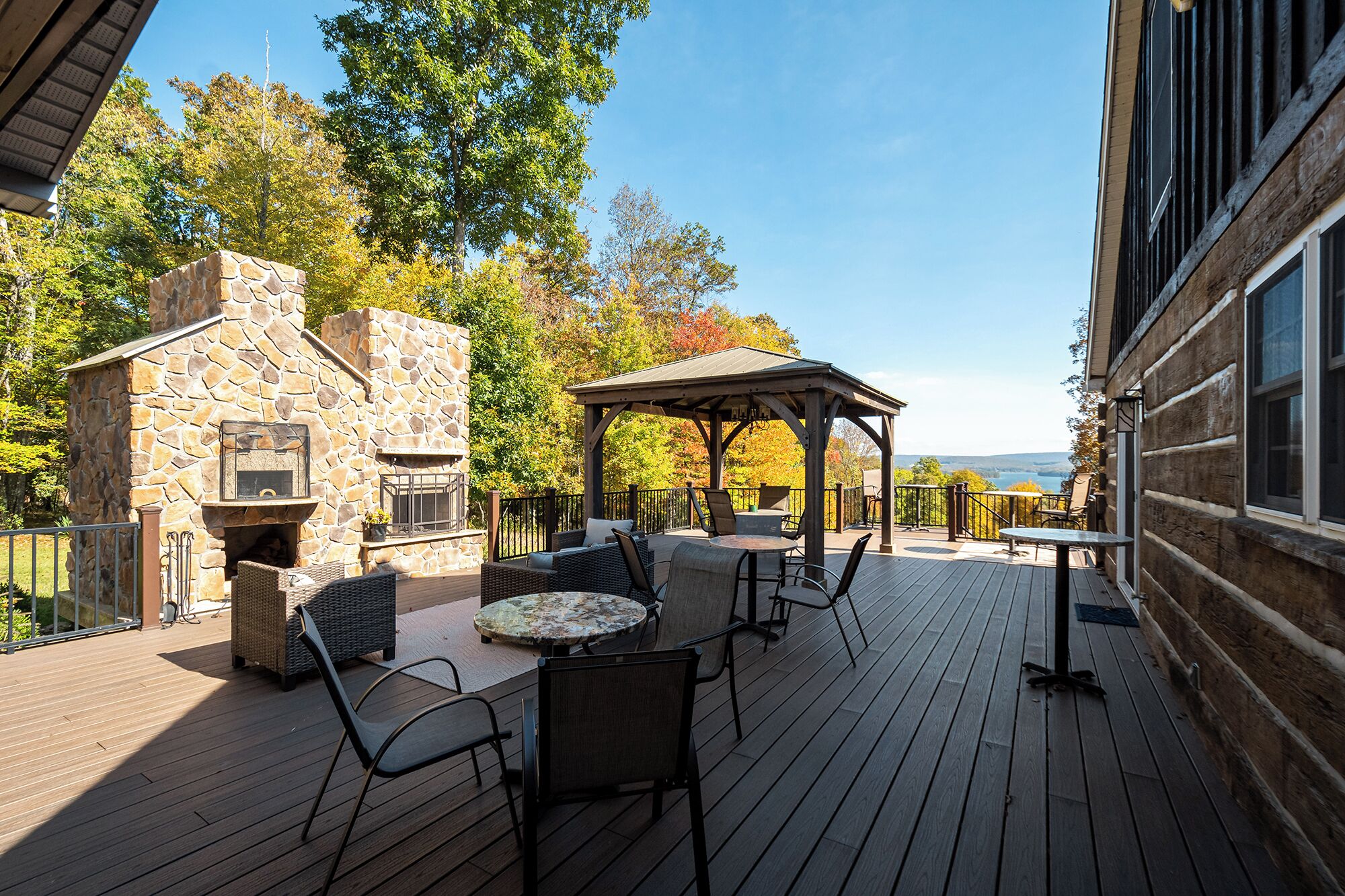 Terraza exterior con chimenea de piedra, asientos cubiertos y vista del paisaje.