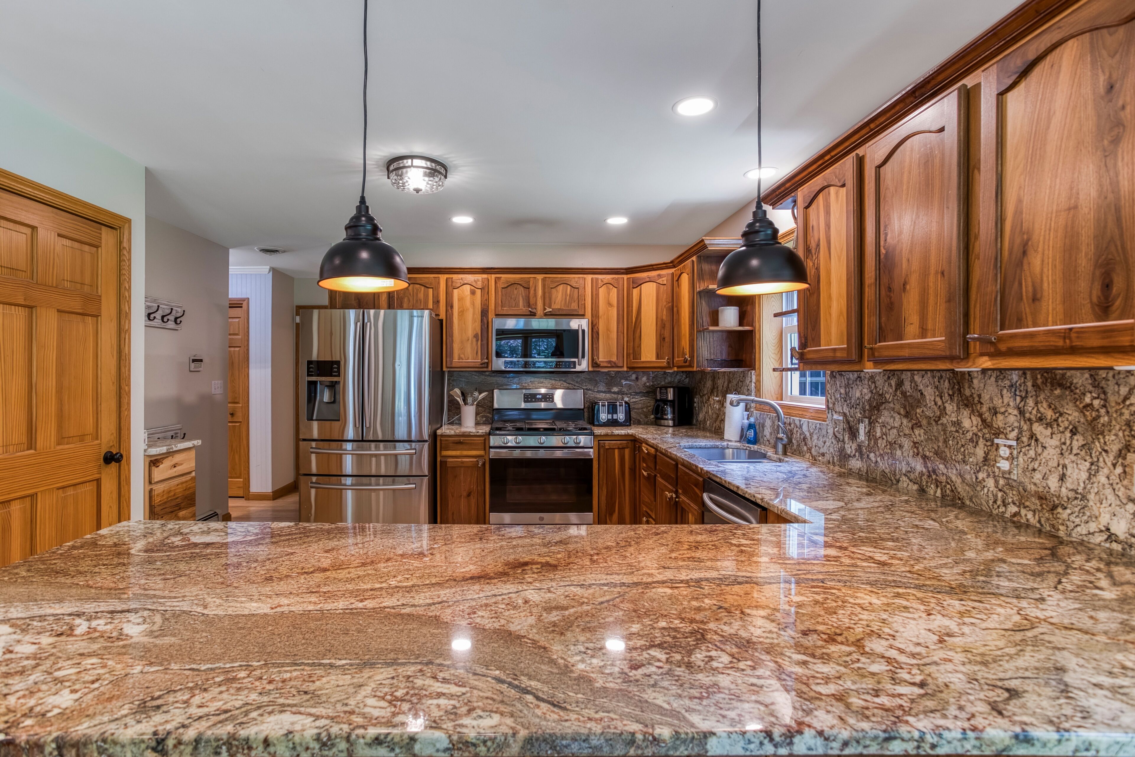A kitchen with granite countertops, stainless steel appliances, wooden cabinets, and pendant lighting.
