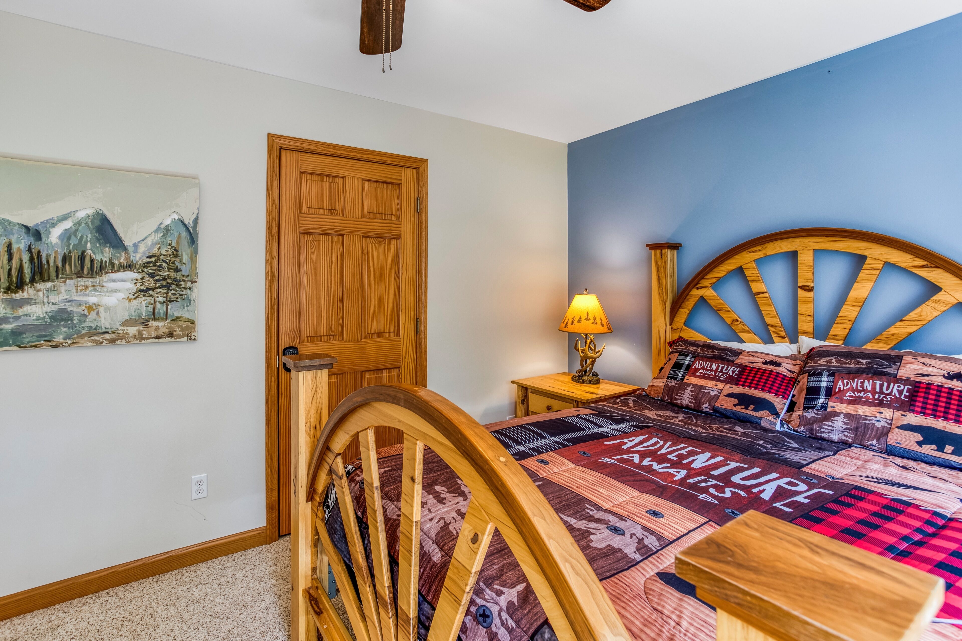 A bedroom with a wooden bed frame, a nightstand with a lamp, a door, and a wall painting.