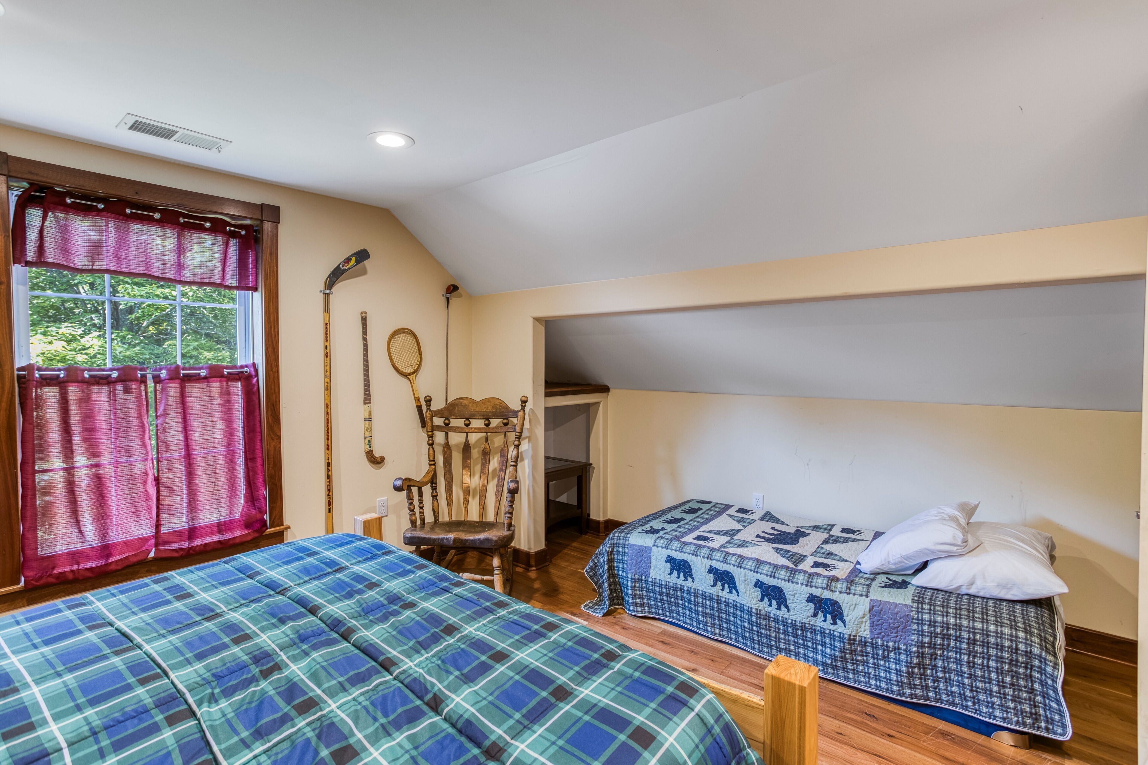 A bedroom with two beds, a window with curtains, a chair, and a hockey stick on the wall.