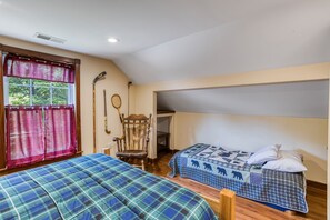 A bedroom with two beds, a window with curtains, a chair, and a hockey stick on the wall.