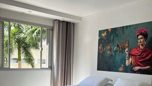 A bedroom with a large bed, a window with curtains, a ceiling light, and a wall painting. - Beautiful apartment in the center of Florianópolis (Centro Florianópolis)
