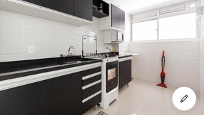 A modern kitchen with black and white cabinetry, a built-in oven, and a window with blinds. - Beautiful apartment in the center of Florianópolis (Centro Florianópolis)