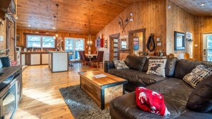 A cozy cabin interior with a wooden interior, a dining area, and a living room with a sofa and a fireplace. - Chalet Le Shack Sur la rouge (La Conception)