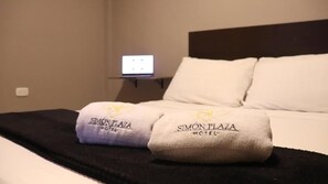 A hotel bed with two towels labeled 'Simon Plaza Hotel' and a laptop on a stand in the background. - Hotel Simon Plaza (Pereira)
