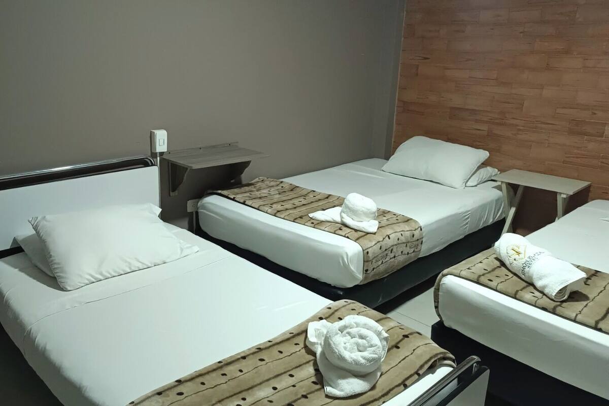 Habitación de hotel con dos camas, una mesita de noche, un ventilador y una pared de ladrillo.