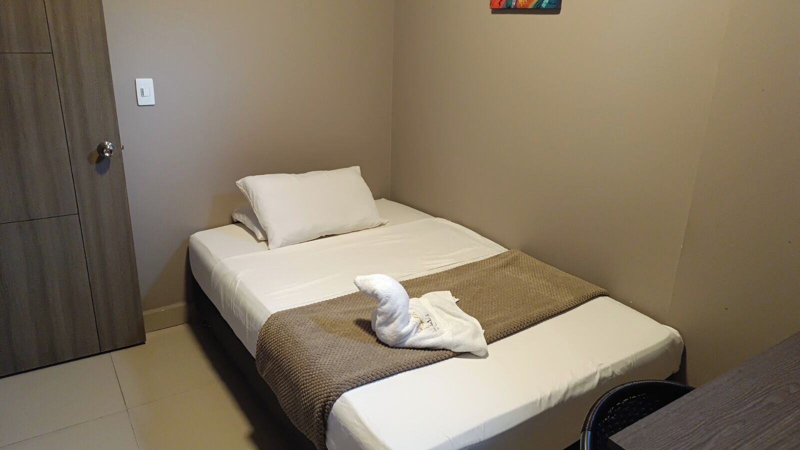Una cama individual con colchón blanco, manta marrón y toalla blanca.