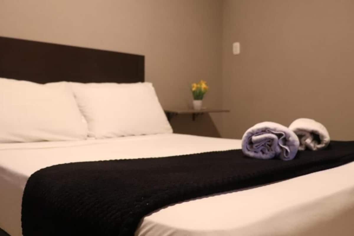 Habitación de hotel con una cama bien hecha, un plaid negro y toallas sobre la cama.