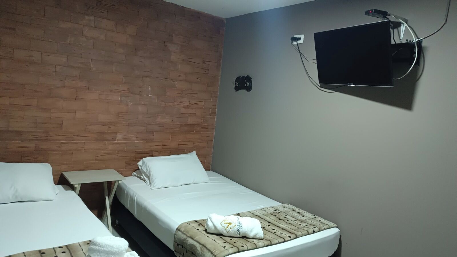 Habitación de hotel con dos camas, un televisor de pantalla plana montado en la pared y un revestimiento de ladrillo.