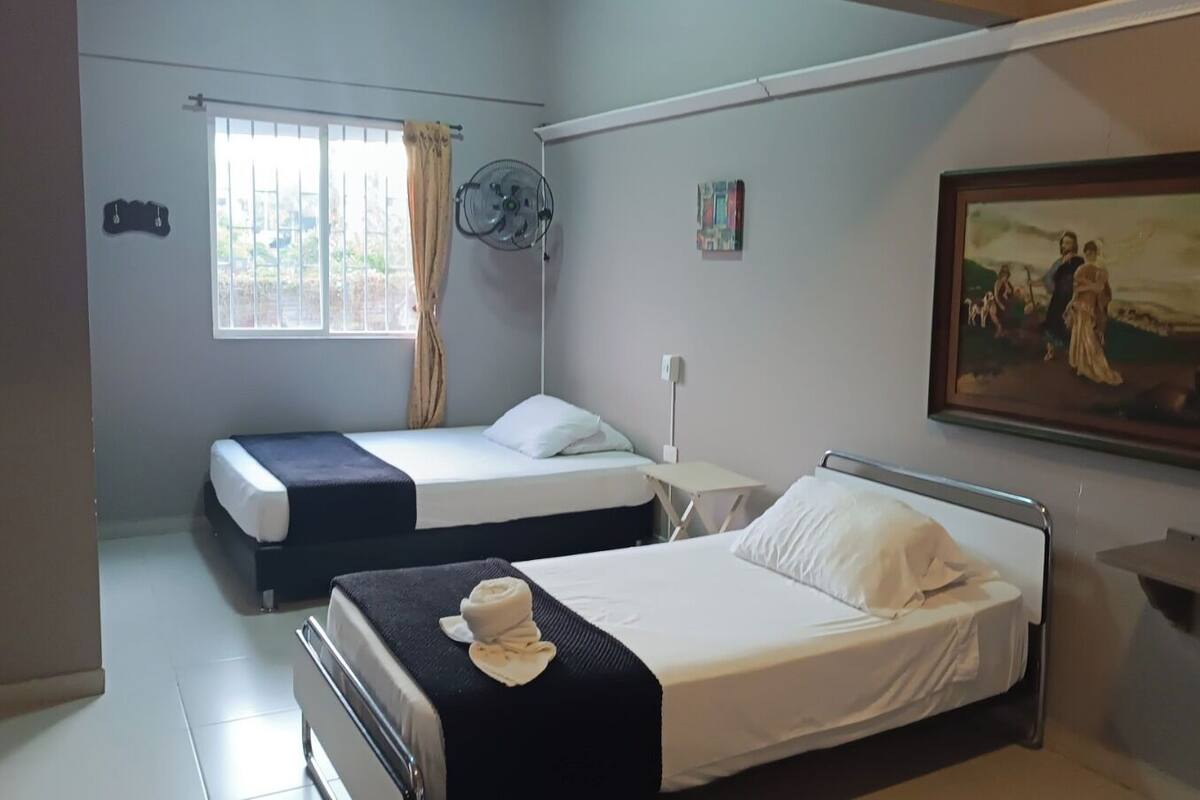 Una habitación de hotel con dos camas, un cuadro en la pared y un ventanal con cortinas.