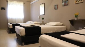 Une chambre d’hôtel avec trois lits, une petite table, un miroir et une fenêtre avec des rideaux.