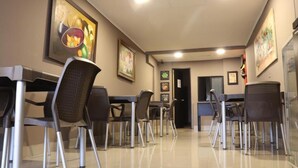 Un espace repas avec des chaises et des tables en métal, des œuvres d’art encadrées accrochées aux murs et une porte visible au fond.