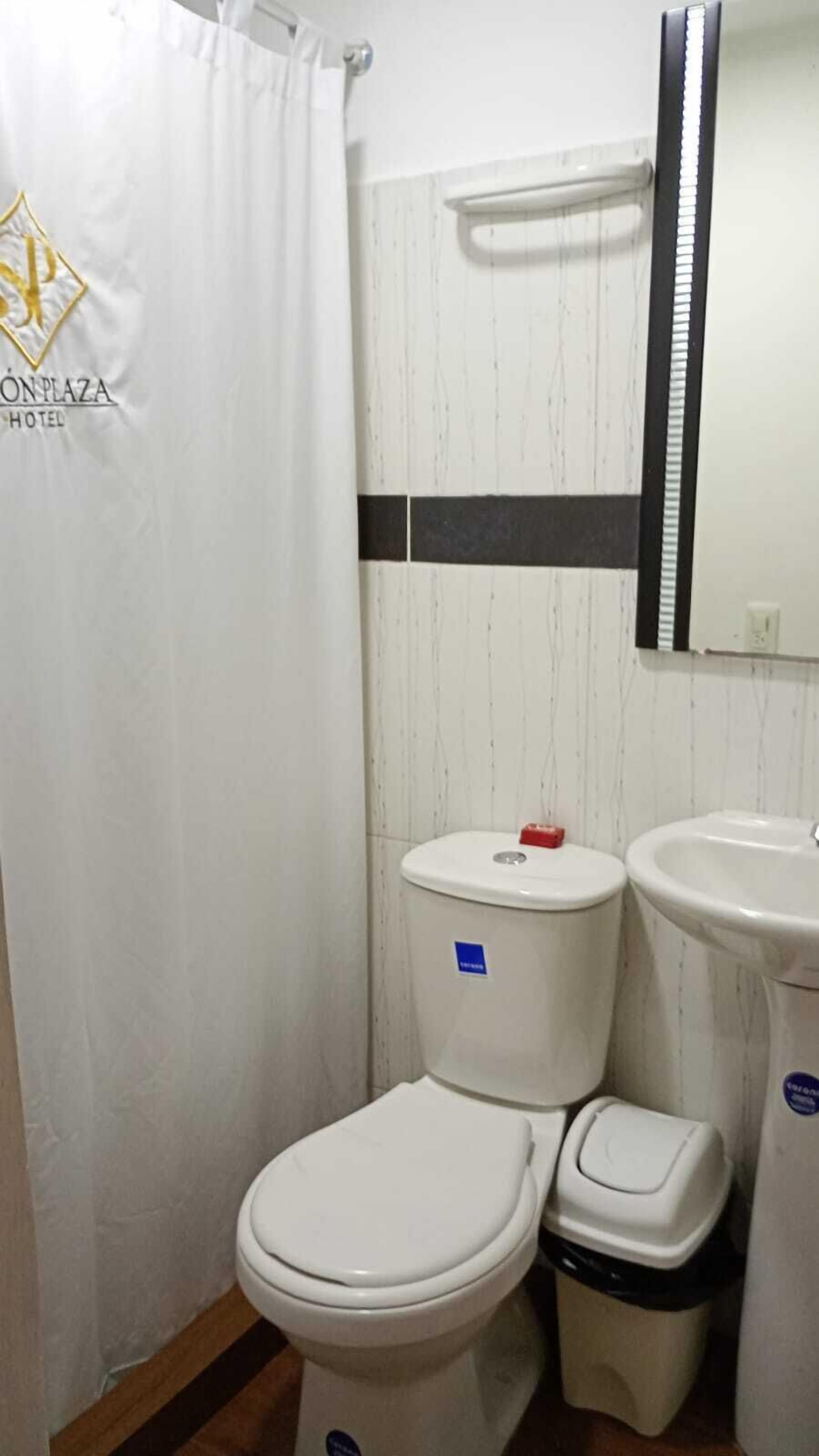 Un bany petit amb un vàter blanc, un bidet i un lavabo. Hi ha una cortina de bany i una tovallola penjant a la paret.