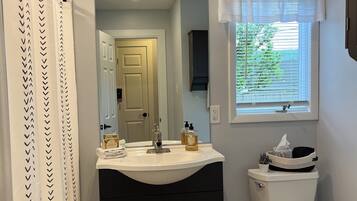 A bathroom with a white sink, dark cabinet, toilet, and a window with a view of greenery.