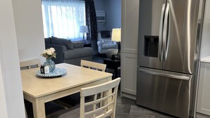 A modern kitchen with a stainless steel refrigerator, a dining table with chairs, and a living area with a sofa and a lamp. - Welcome to the Moravian! (Allentown)