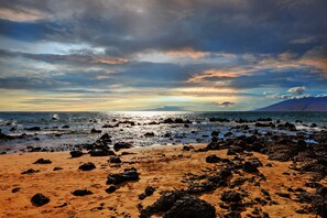 A beach with rocky terrain and a view of the ocean under a cloudy sky.