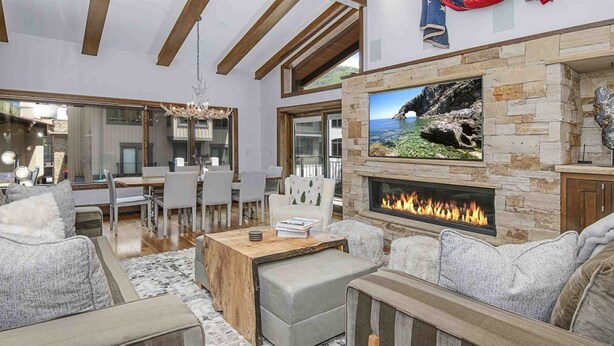Un salon spacieux avec une cheminée en pierre, des meubles modernes et une grande fenêtre donnant sur un paysage magnifique.