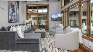 Un salon avec un canapé gris, un fauteuil blanc et un téléviseur fixé à un mur en bois.