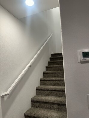 Una escalera con peldaños alfombrados, paredes blancas y barandilla.